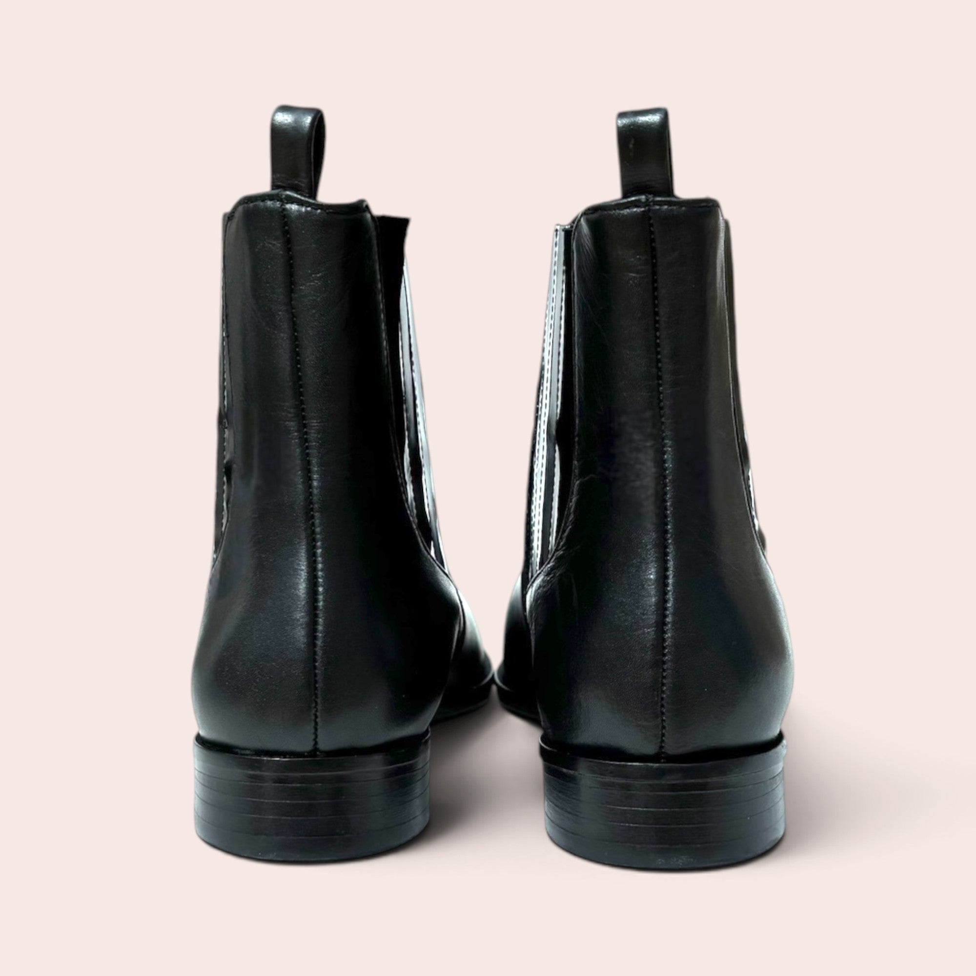Back view of black leather Chelsea ankle boots with pull tabs and low heels on a light background