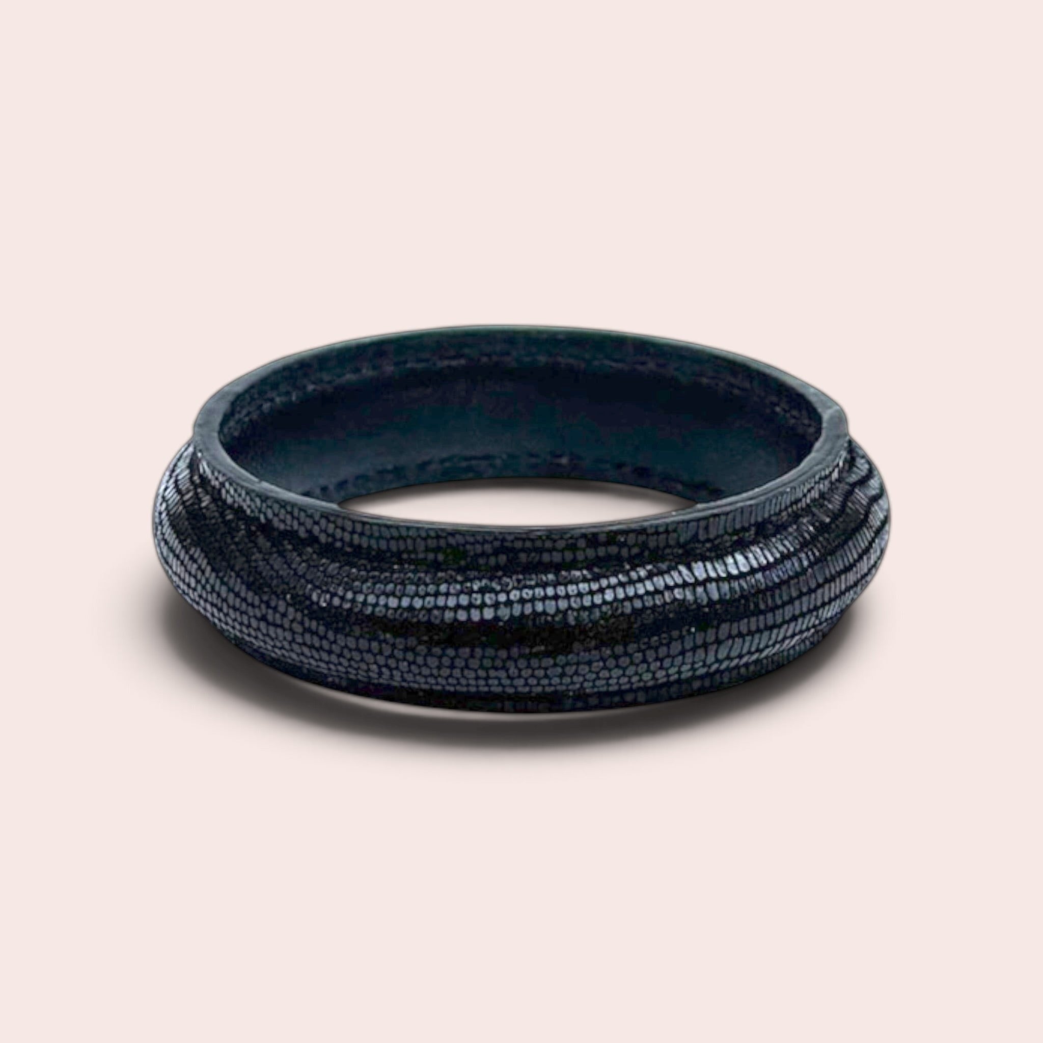 Black suede leather bangle bracelet with a textured lizard-skin embossed pattern on a light background.