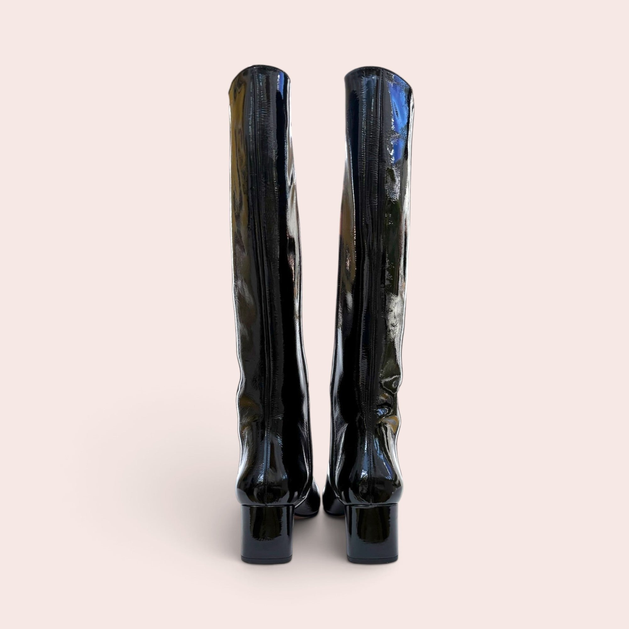 Back view of black patent leather knee-high boots featuring a sturdy block heel and a full-length side zipper.
