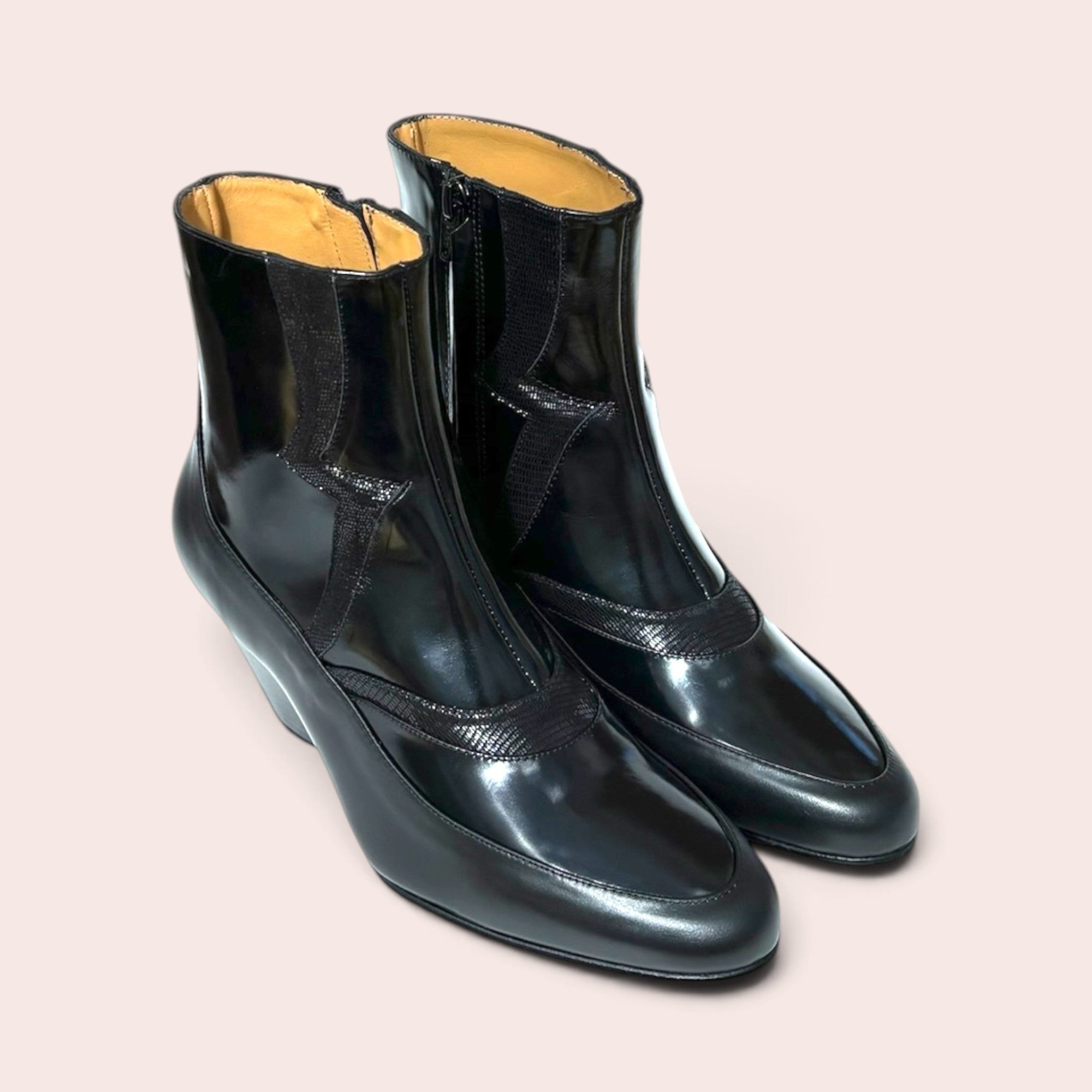 Pair of black high-shine ankle boots with a pointed toe, sculptural heel, and western-inspired textured paneling.