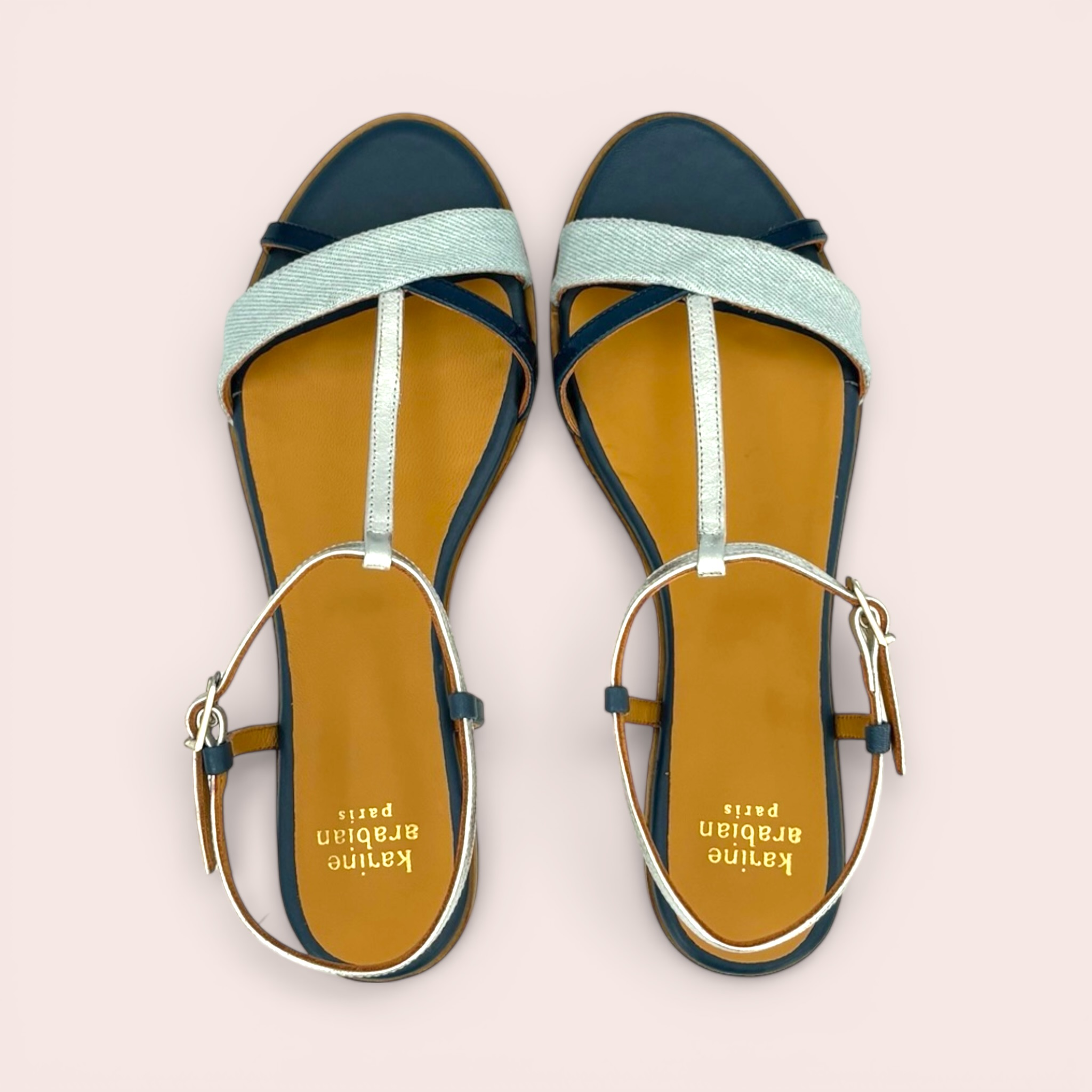 Flat sandals with navy blue leather trim, light blue denim straps, and silver accents. Features a T-strap design and adjustable ankle strap.