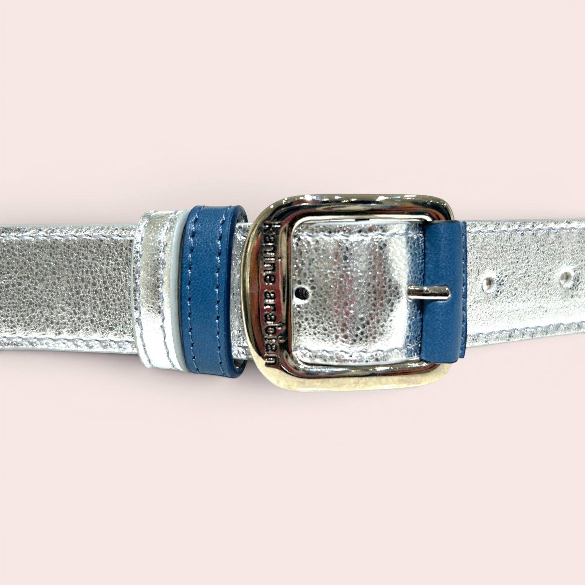 Ceinture fine en cuir argenté métallisé texturé avec boucle carrée argentée et passant bleu marine. Marque Karine Arabian.