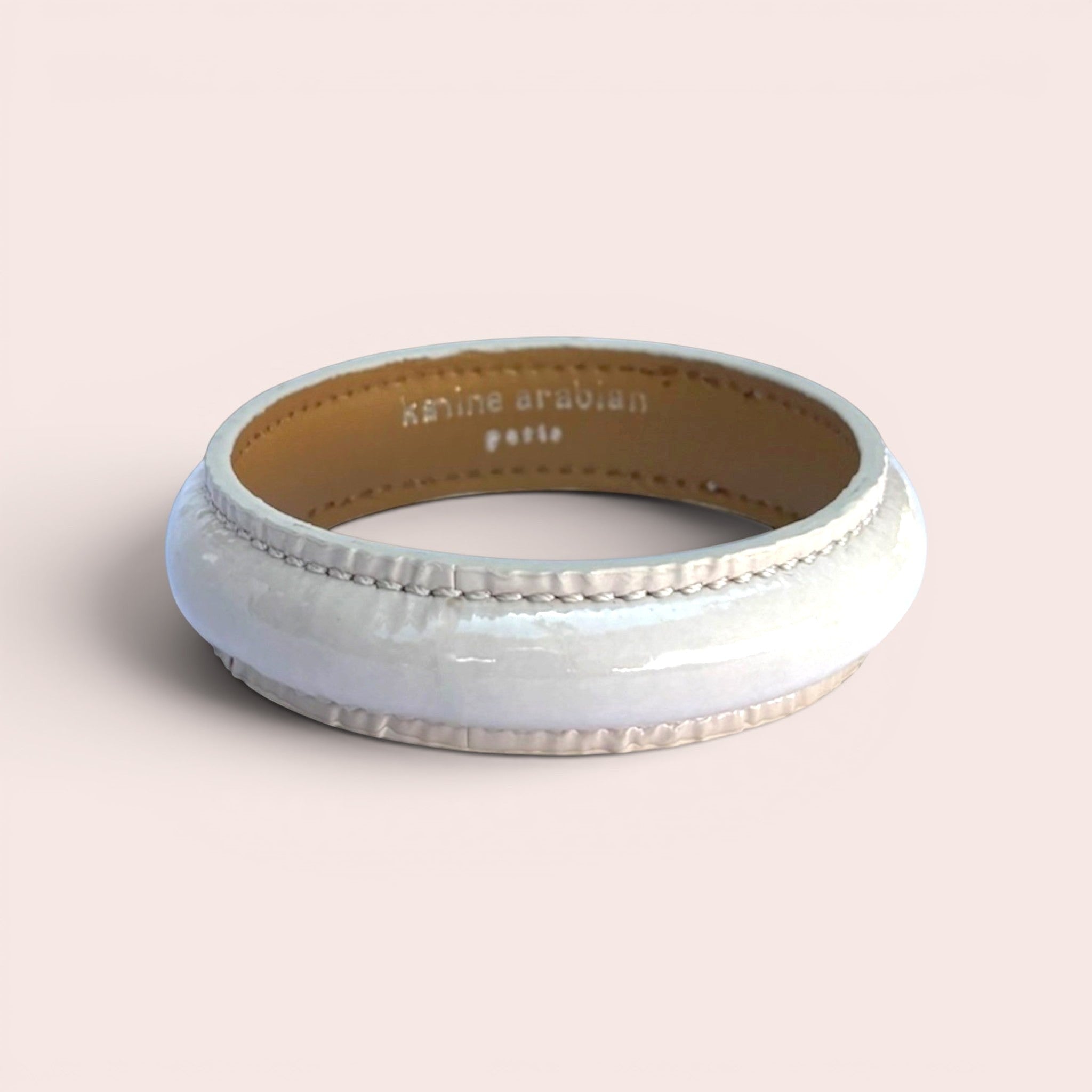 Cream patent leather bangle bracelet with stitched detailing and Karine Arabian Paris branding on the inner lining.