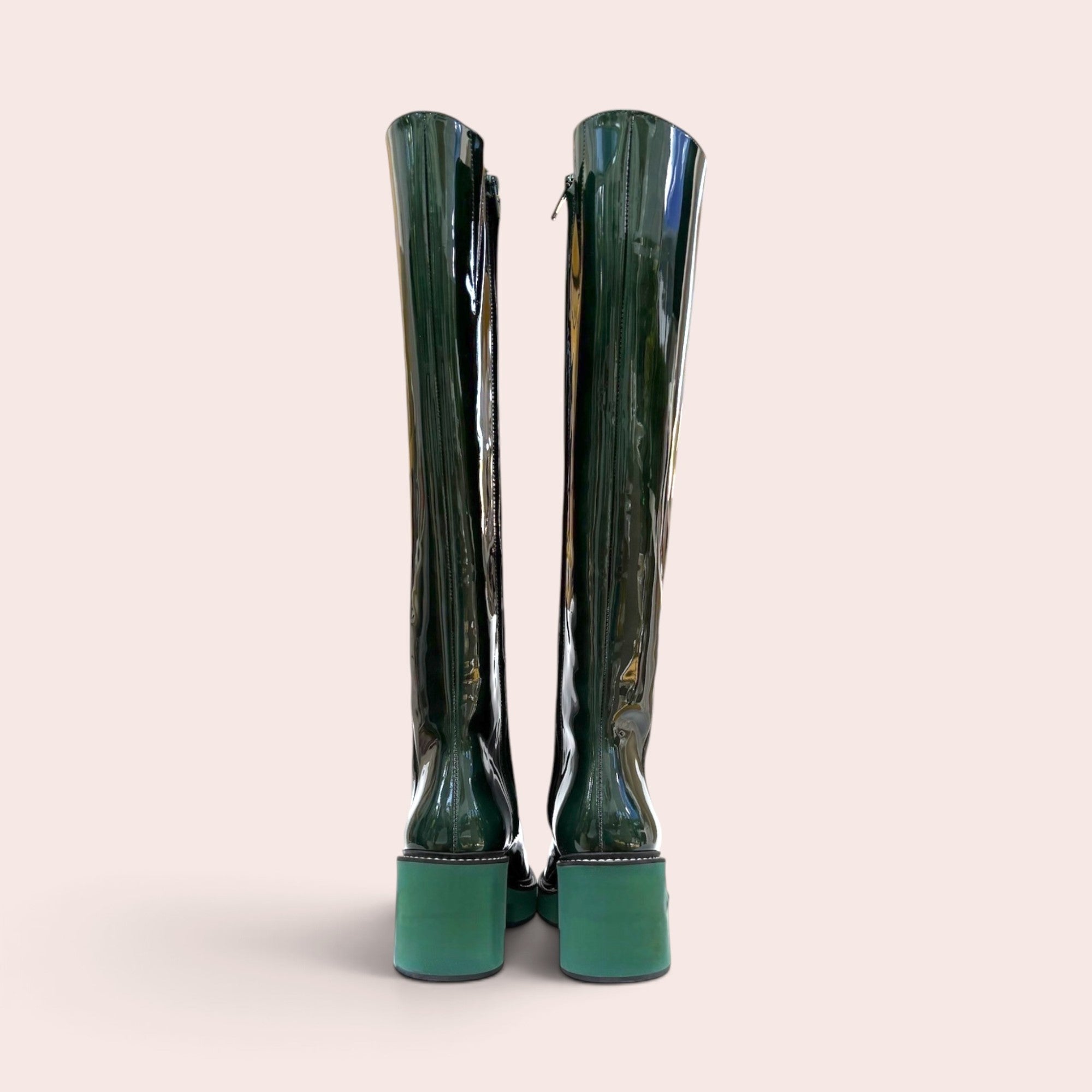 Back view of forest green patent leather knee-high boots with contrasting light green block heels and side zippers.