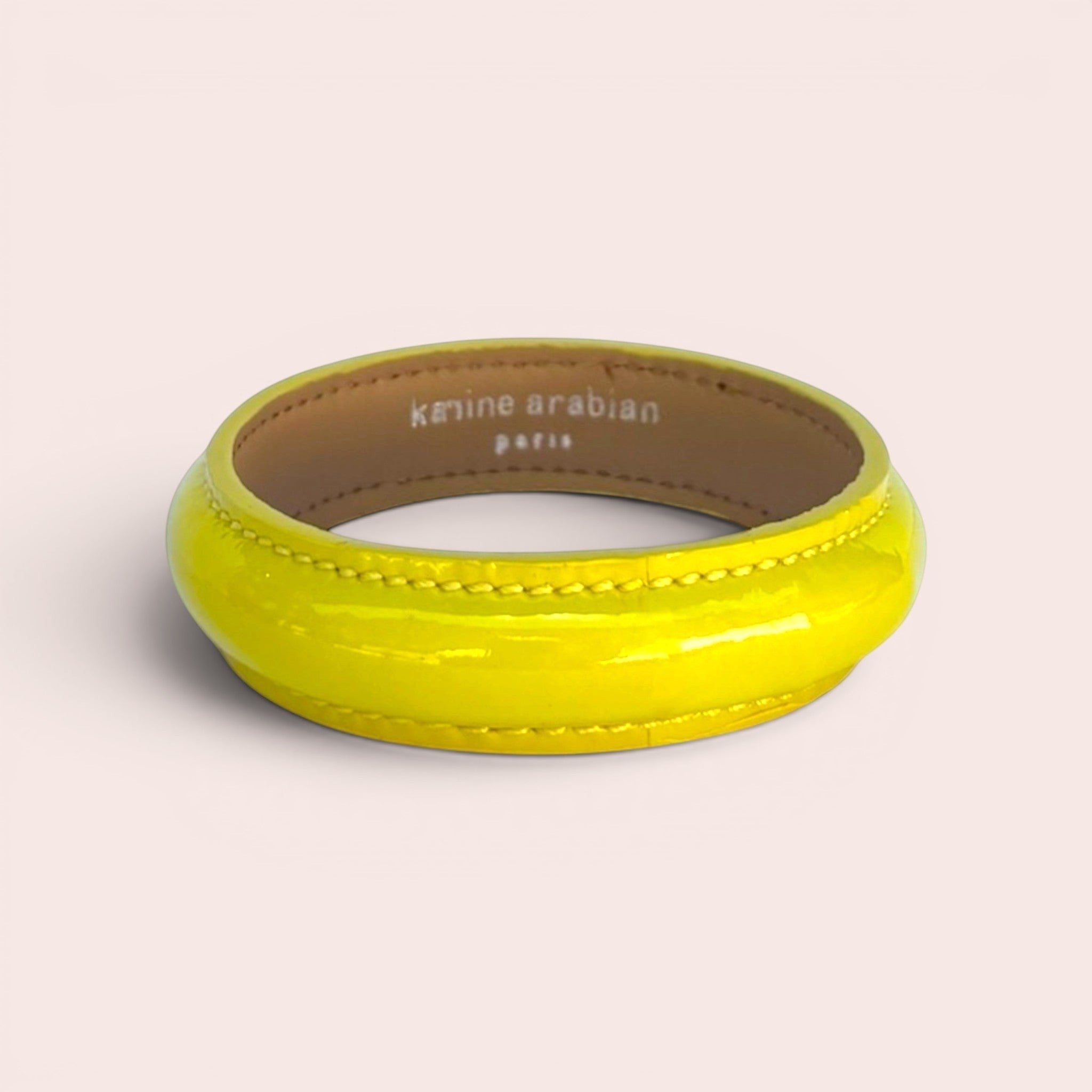Lemon yellow patent leather bangle bracelet with visible stitching and Karine Arabian Paris branding on the interior.