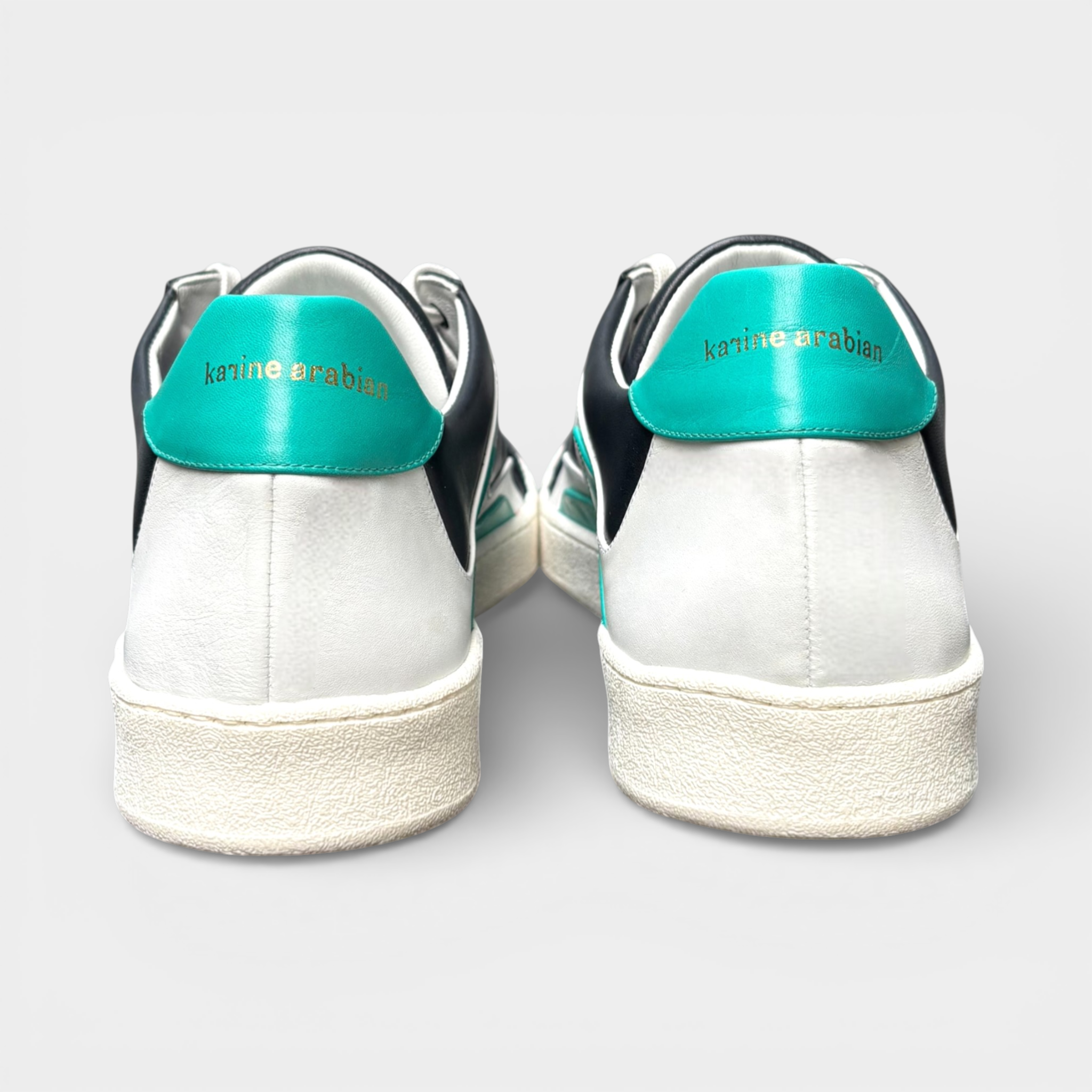 Men's black and white leather sneakers with teal heel accents and gold 'karine arabian' branding.