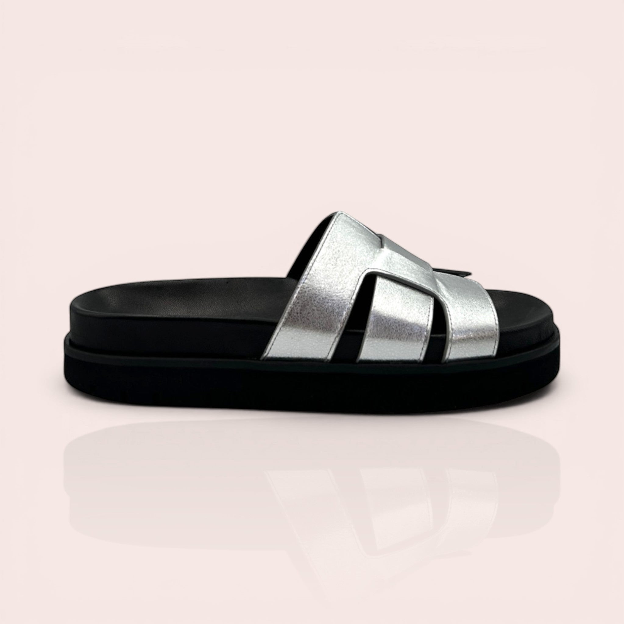 Silver metallic leather mule sandal with interwoven straps and a black platform sole. Designed for comfort and style.