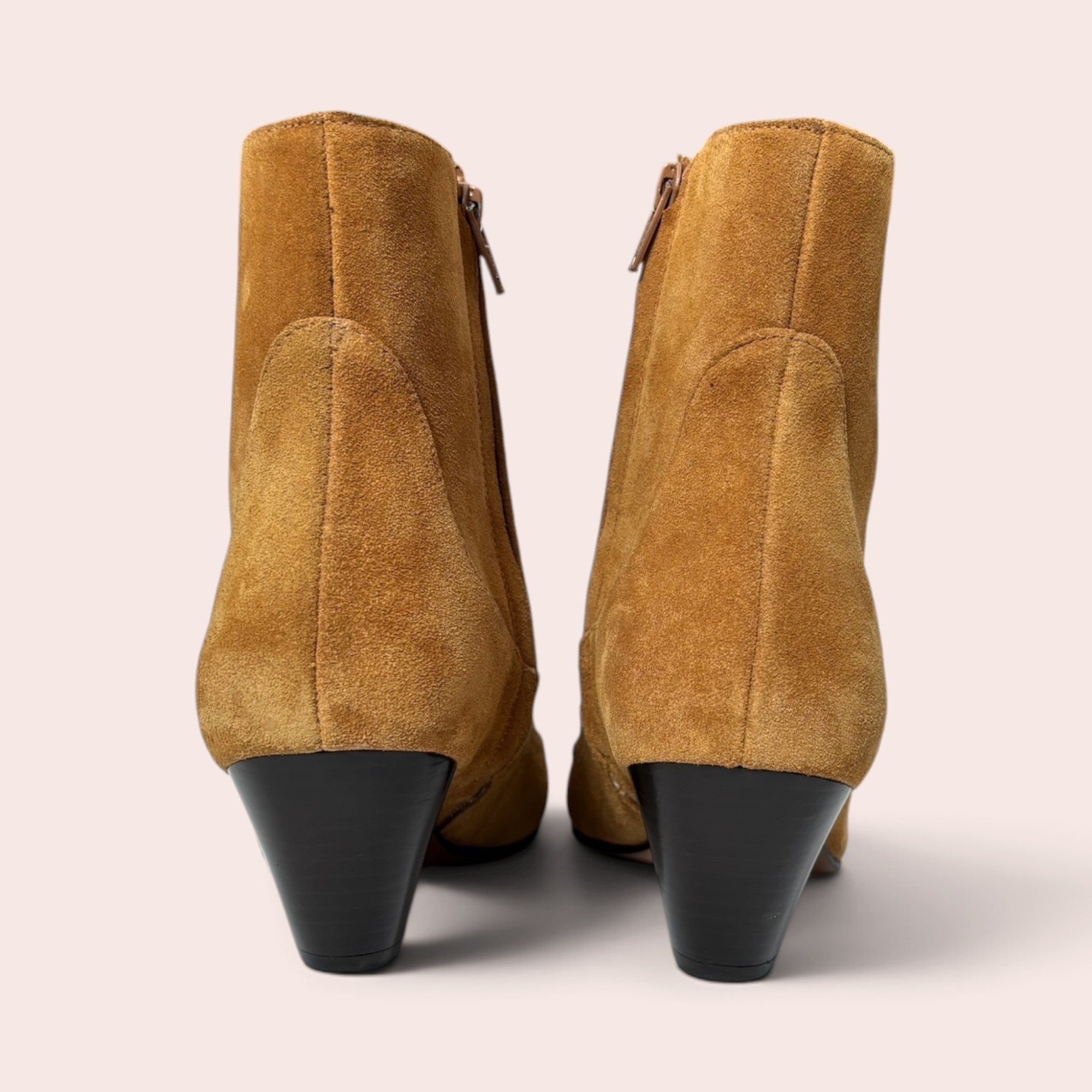Rear view of tan suede ankle boots with a sculptural black heel and side zipper closure on a light background.