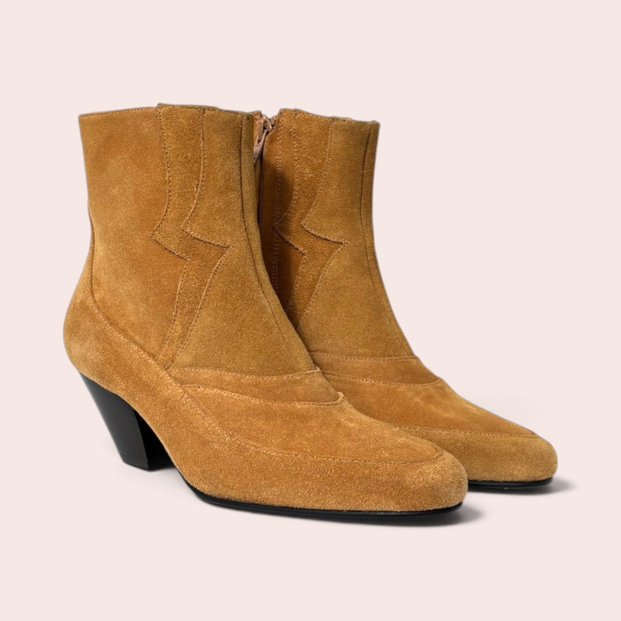 Tan suede ankle boots with western-inspired stitching, pointed toe, and a black sculptural heel against a neutral background